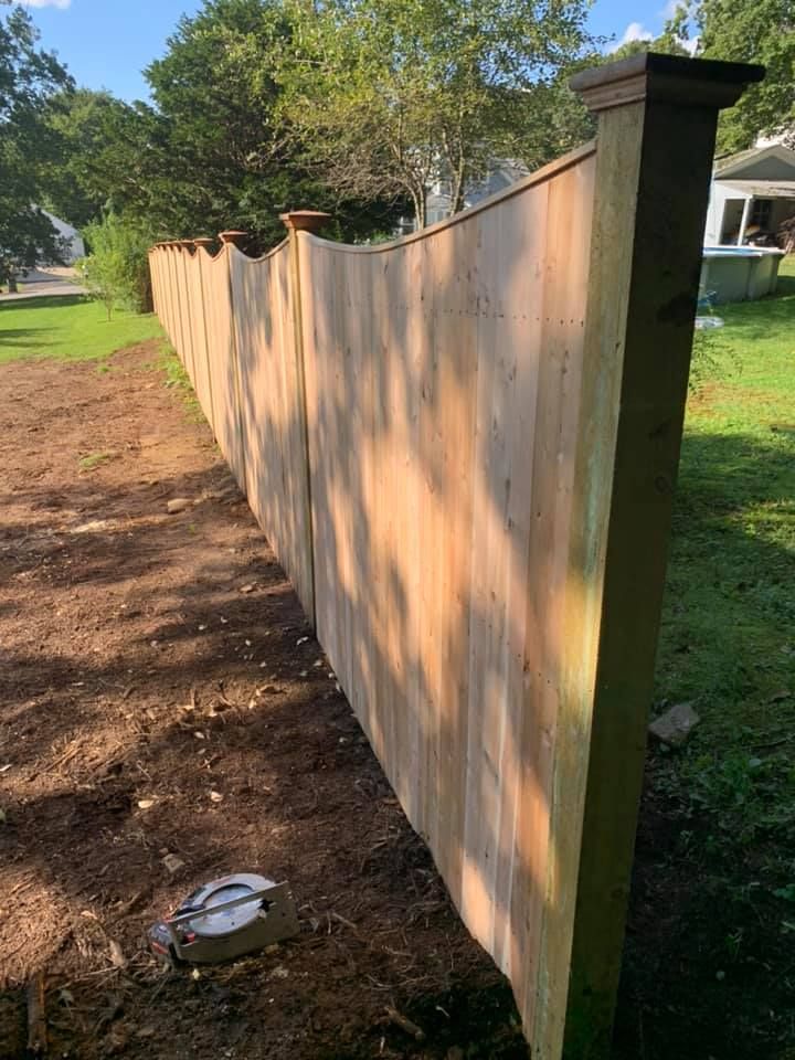 A newly installed wooden privacy fence with a scalloped top edge, viewed at an angle in a residential yard.