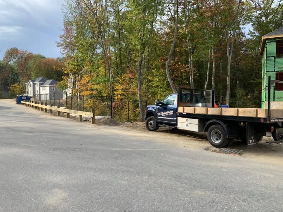 A dark flatbed truck parked on a road next to a newly built wooden retaining wall near a construction site.