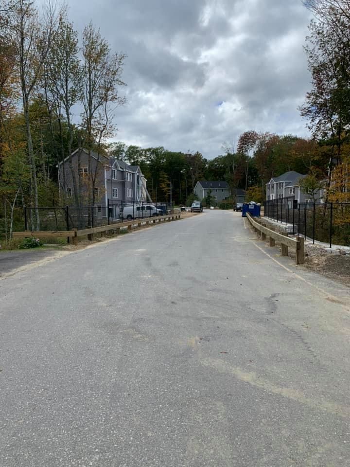 A paved road leads through a residential construction area with light-colored buildings under a cloudy sky.
