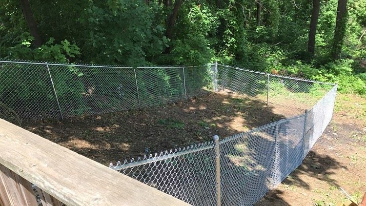 An enclosed dirt yard surrounded by a chain-link fence, viewed from an elevated wooden deck in a wooded setting.