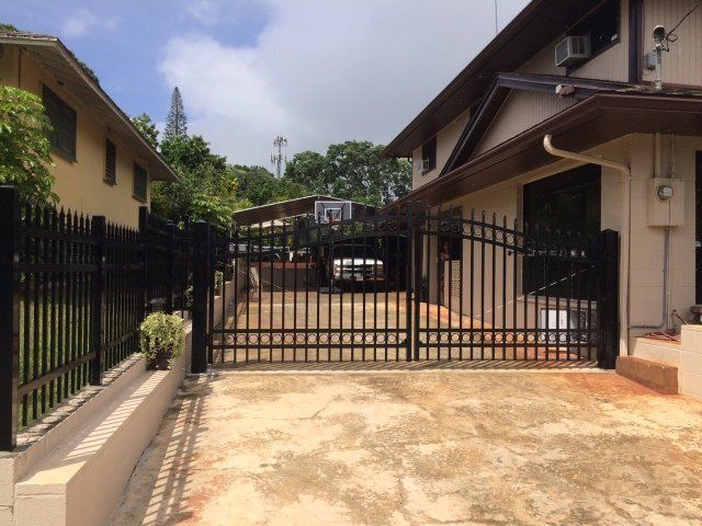 Black gate in front of driveway, beige and brown houses on either side, overcast sky.