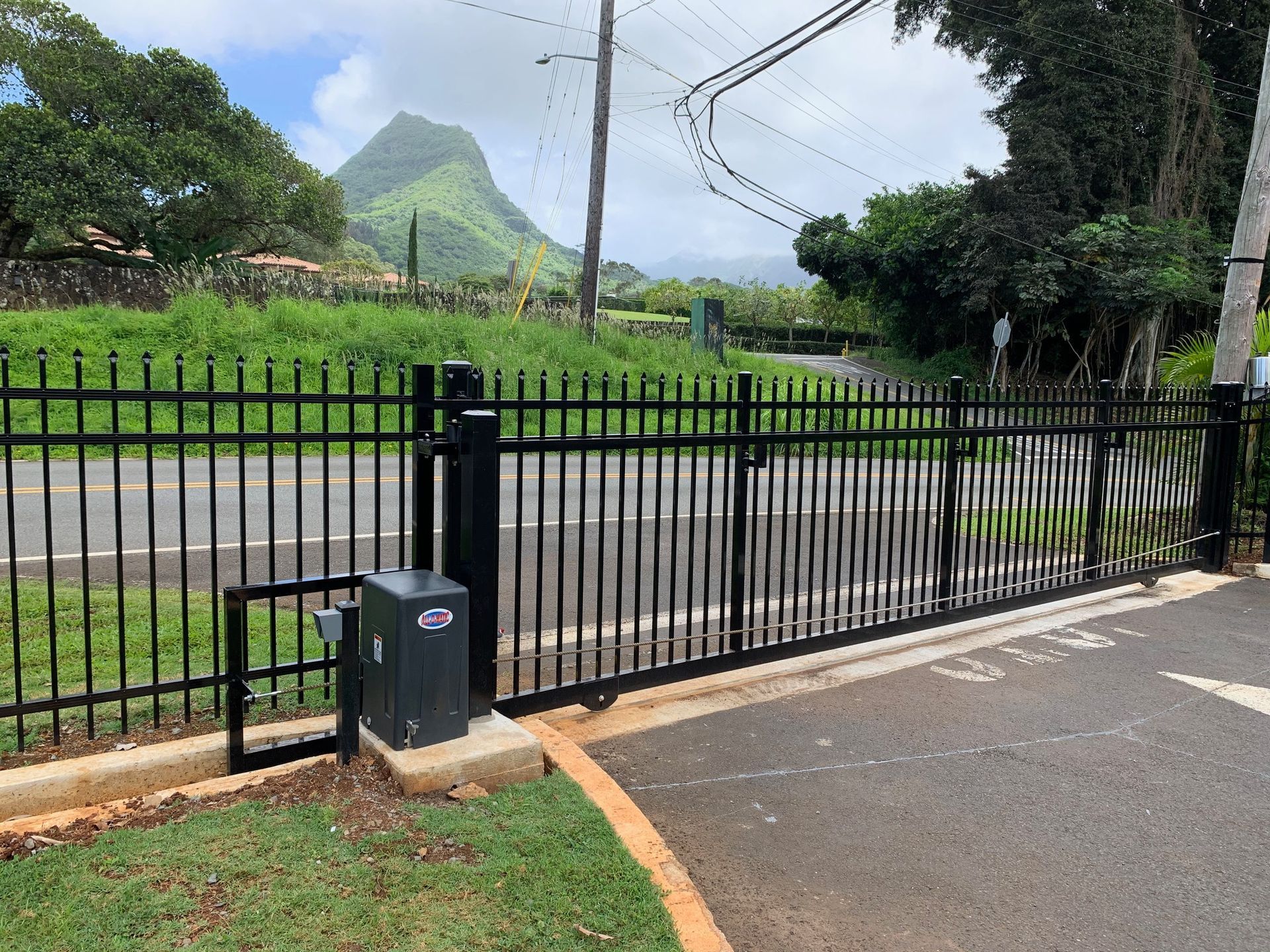 Chain-link fence with a rolling gate on a paved area, beside a building with windows, under a blue sky.