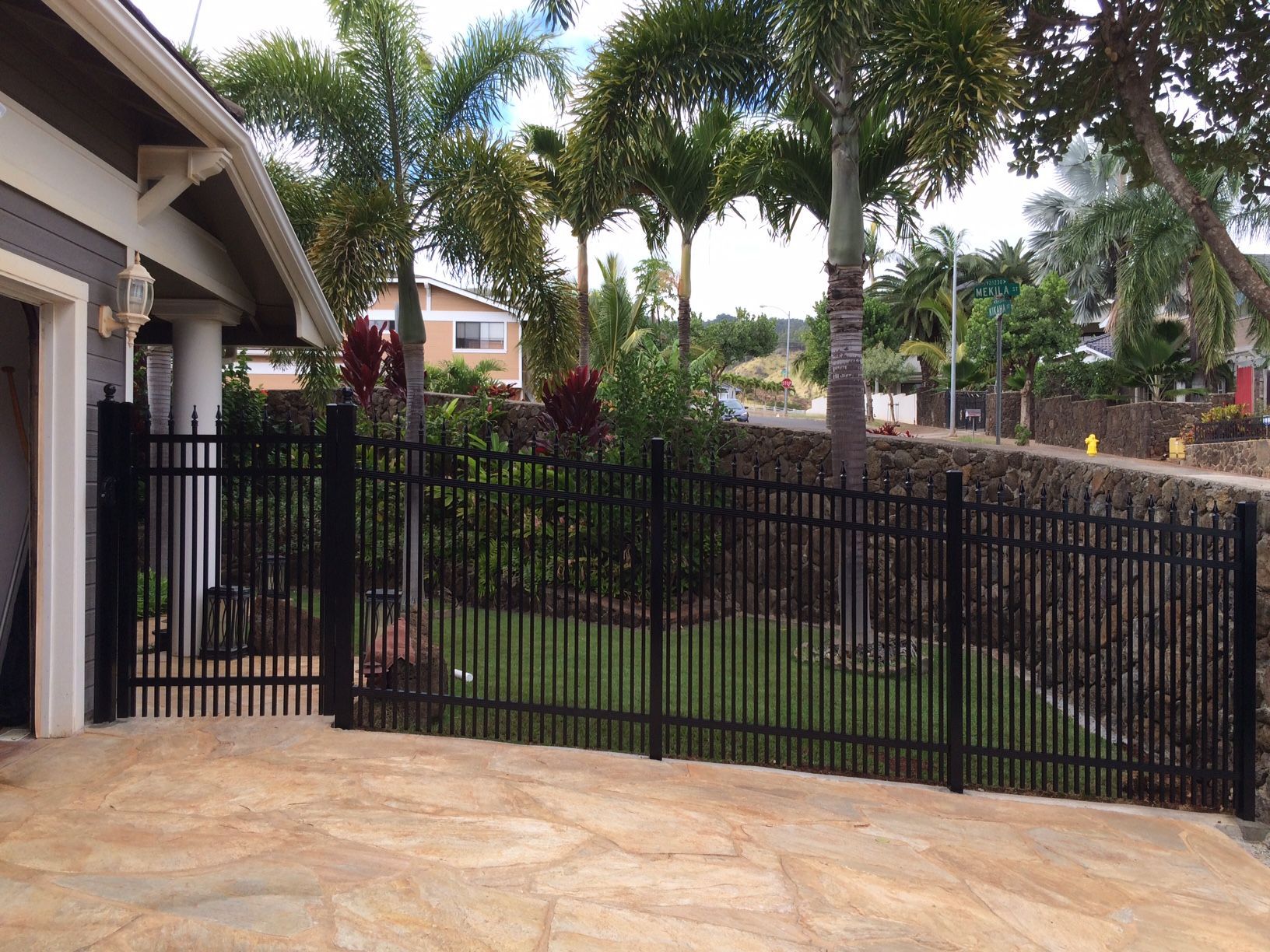 Colorful plants and black fence in front of a building with a white exterior.