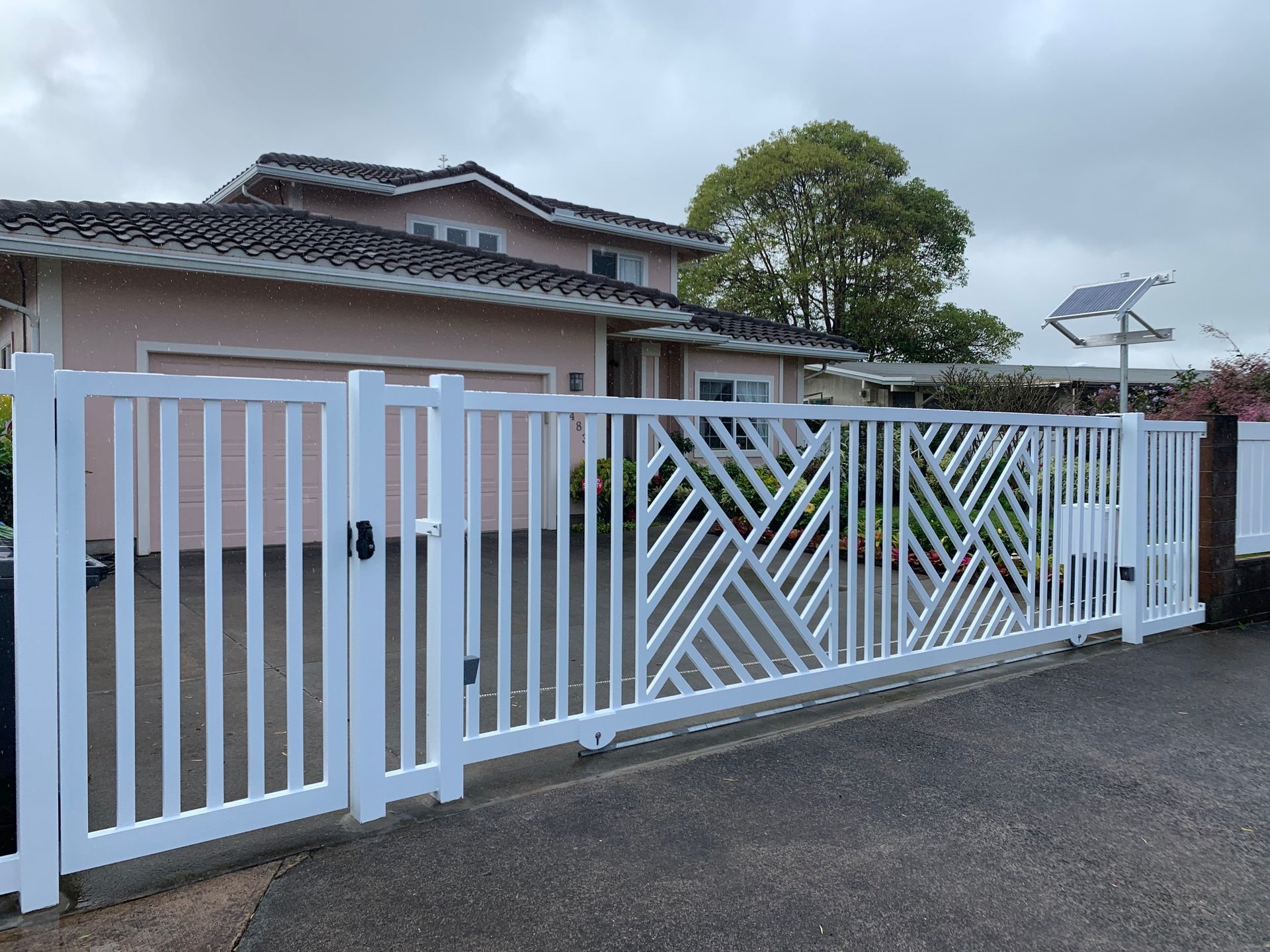 White gated driveway leading to a two-story house with a tan exterior and a cloudy sky.