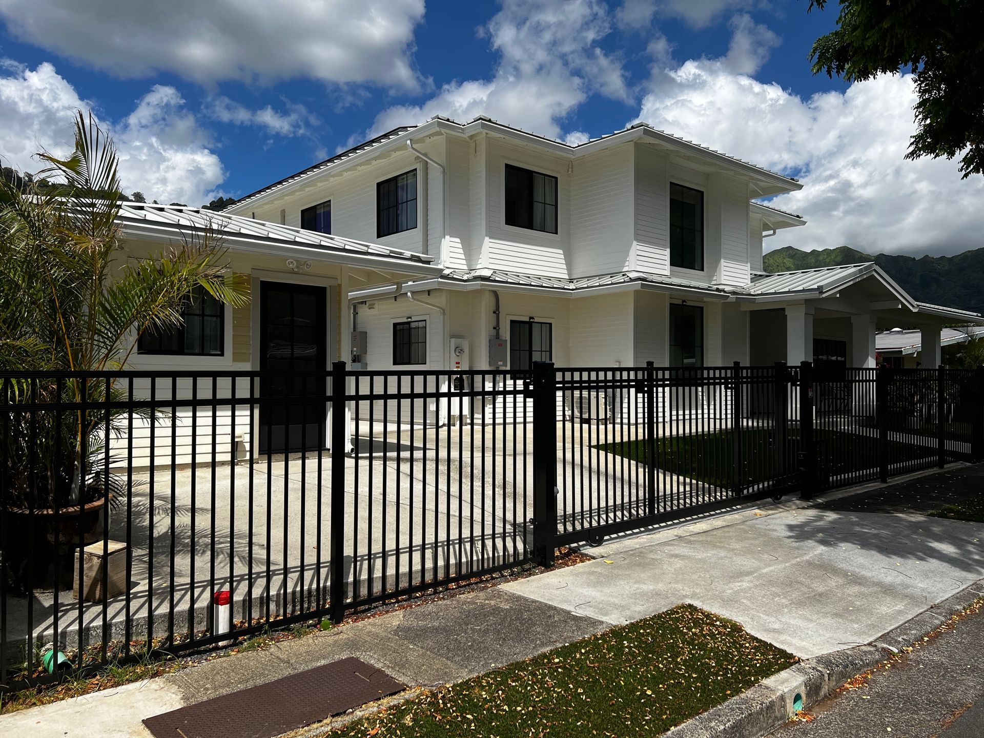 White two-story house with black fence and a blue sky with clouds.