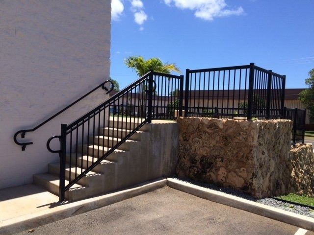 Black metal handrails and fence on concrete stairs, against a stone and white building.