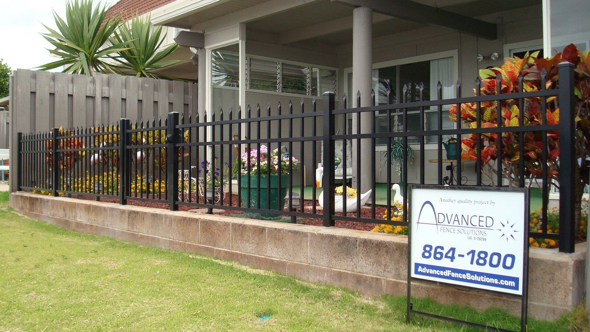 Black aluminum fence in front of a house. Sign shows a company's name and phone number.