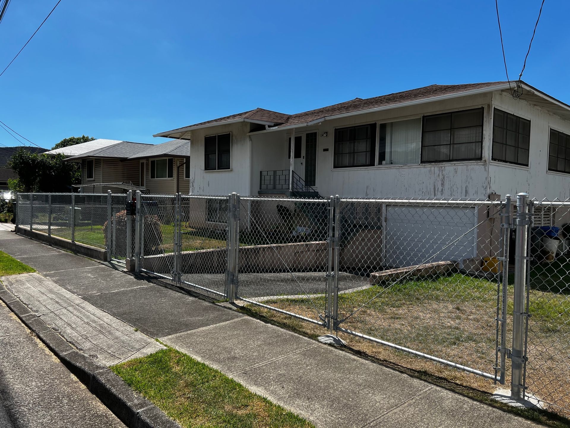 White house with chain link fence, blue sky, and sidewalk.