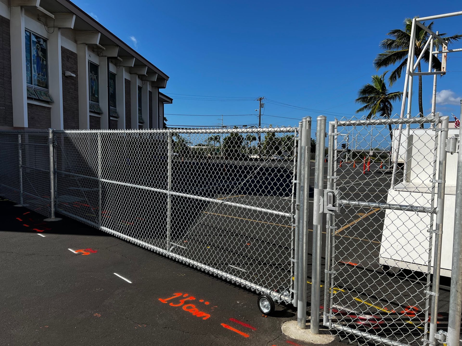Chain-link fence with a rolling gate on a paved area next to a building on a sunny day.