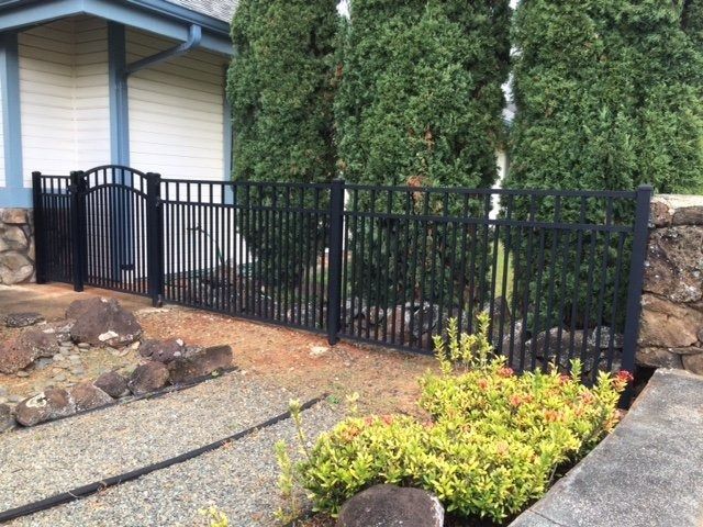 Black metal fence surrounding a garden bed next to a house.