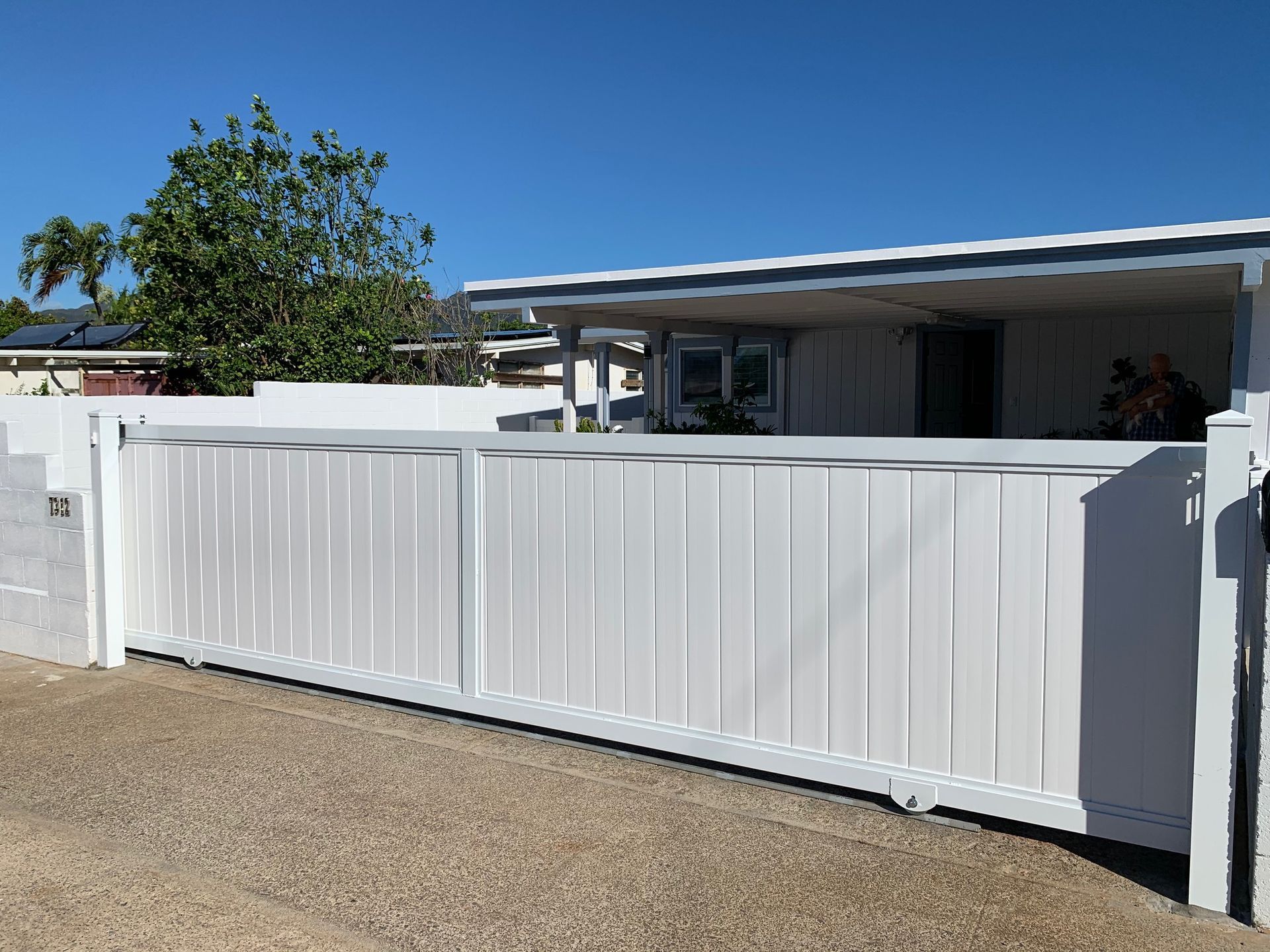 White sliding gate in front of a white house with a blue sky.