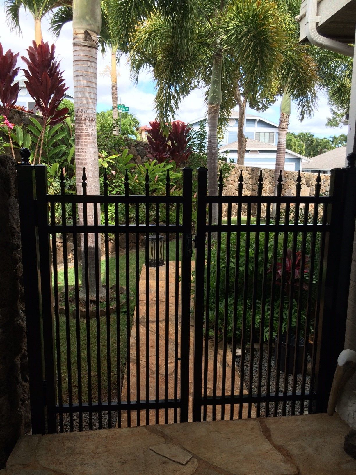 Black wrought iron gate leading to a garden path, flanked by stone walls and lush greenery.
