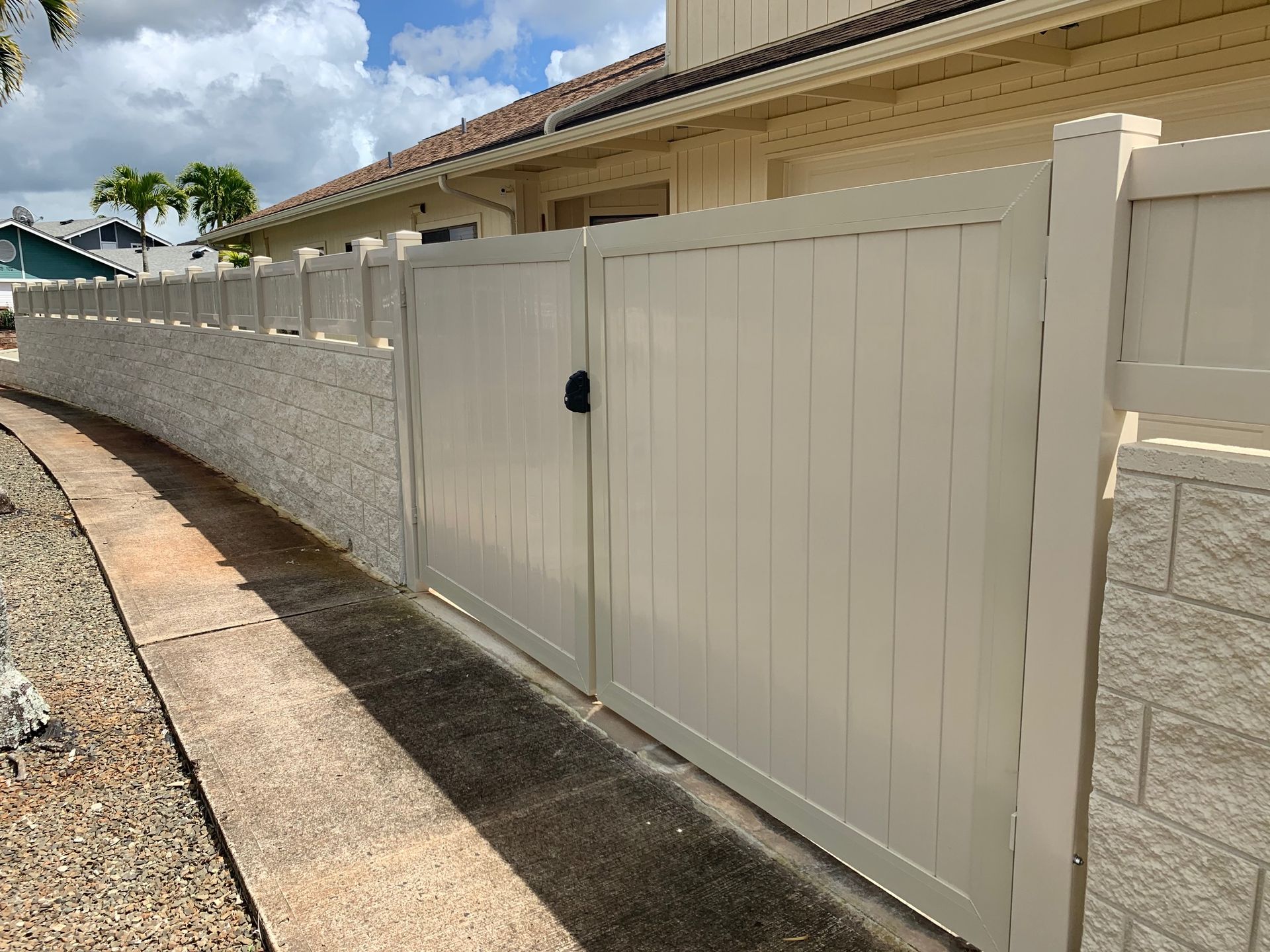 Beige gate in front of a house, set on a stone wall. Pathway curves away on the left.