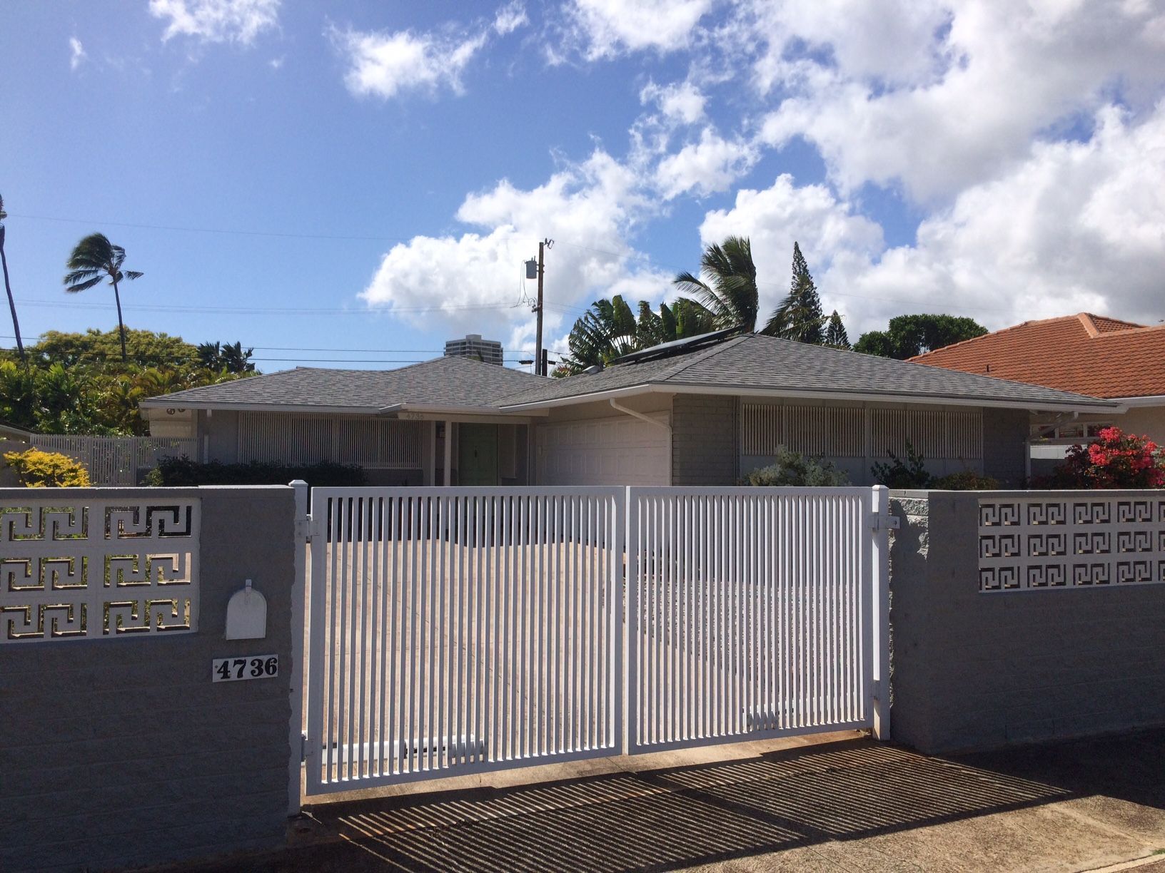 Gray house with white gate and fence on a sunny day.
