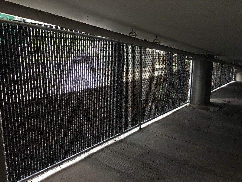 Black chain link fence along a concrete walkway, likely in a parking structure.