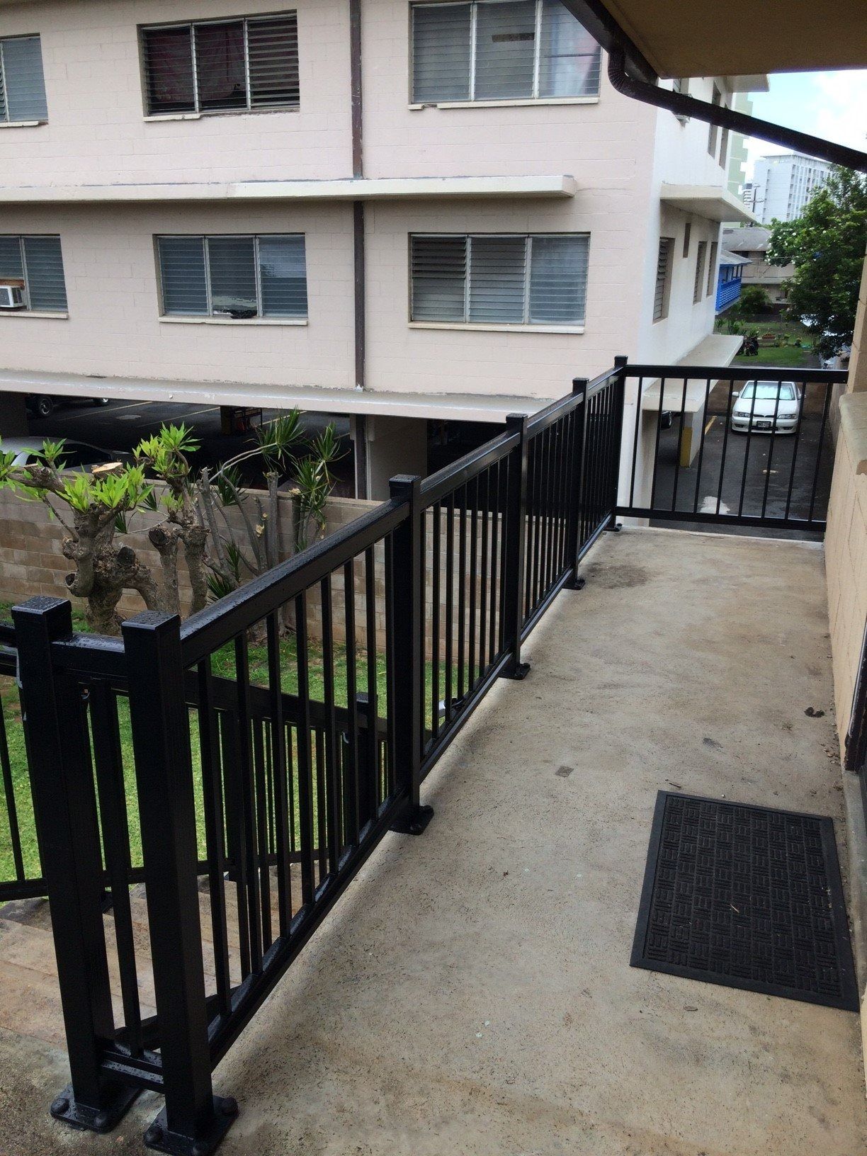 Black metal gate with pointed tops, leading to a garden path with palm trees.