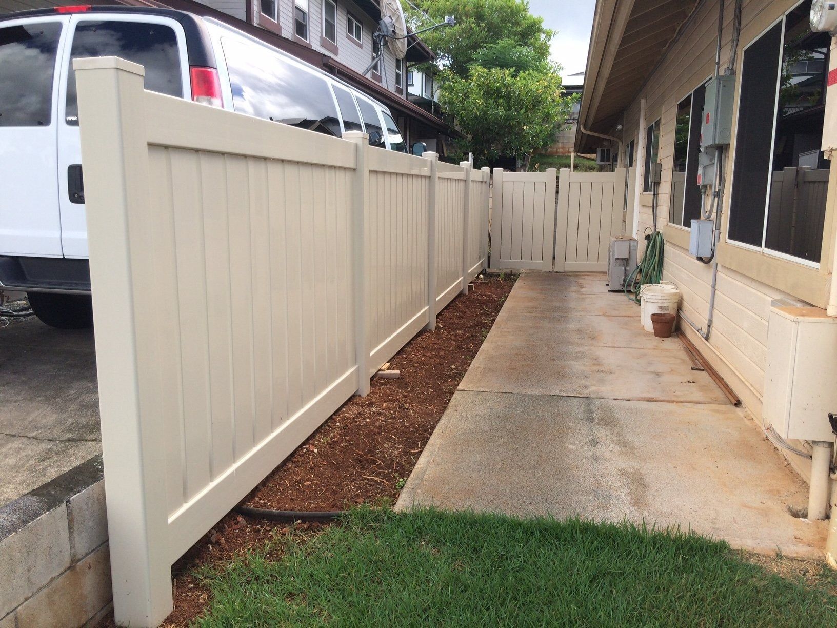Tan vinyl fence alongside a concrete path, leading to a gate and house. A van is parked on the left.