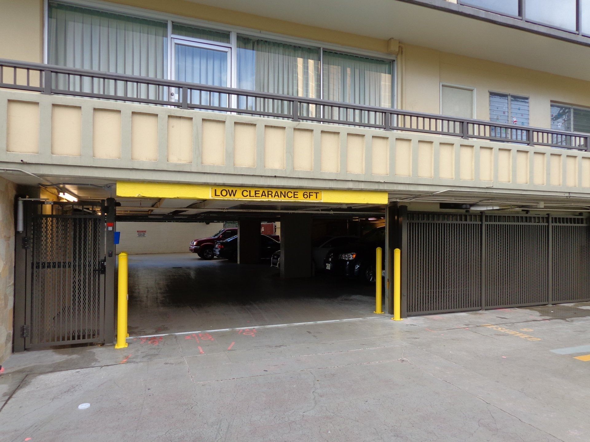 Entrance to a parking garage with a yellow height clearance bar. Two gates are open, revealing a car inside.