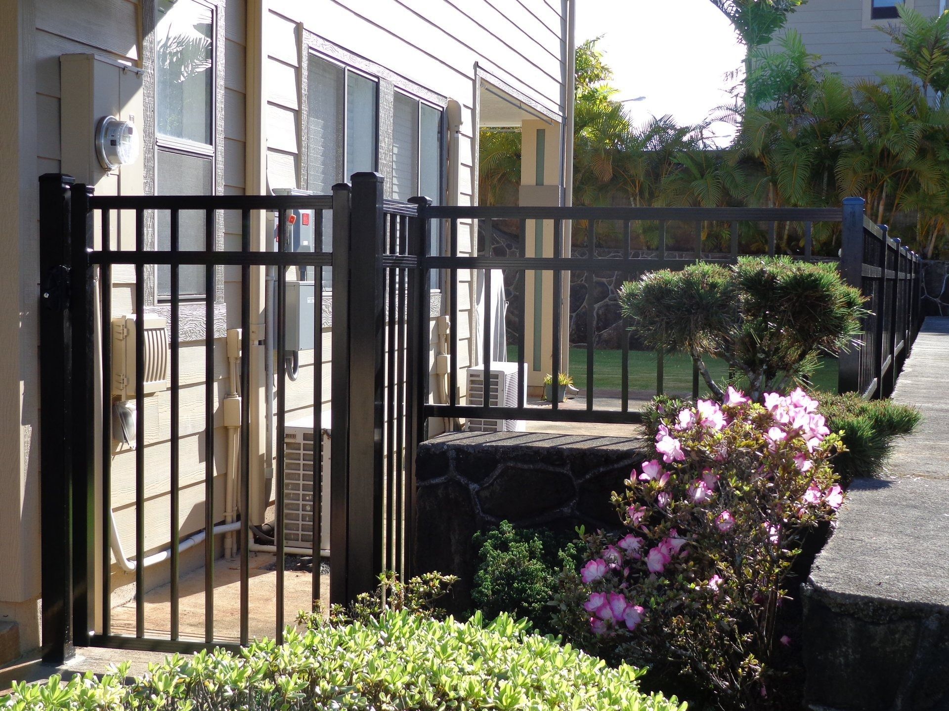 Black metal fence next to a house with a bush and concrete step.