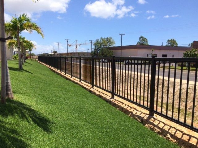 Black metal fence along a grassy strip next to a road, under a blue sky.
