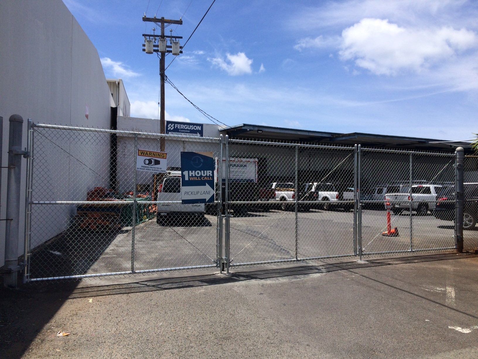 Chain-link fence with a gate, leading to a parking lot. White vans and a sign are visible behind the fence.