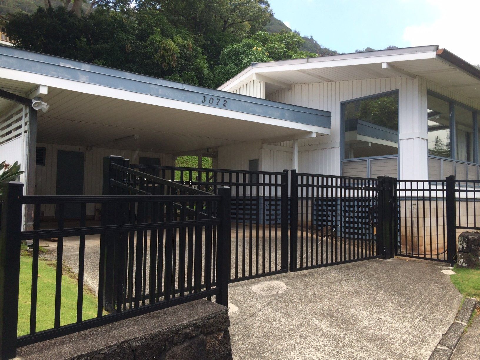 White building with blue roof, black fence, and concrete driveway.