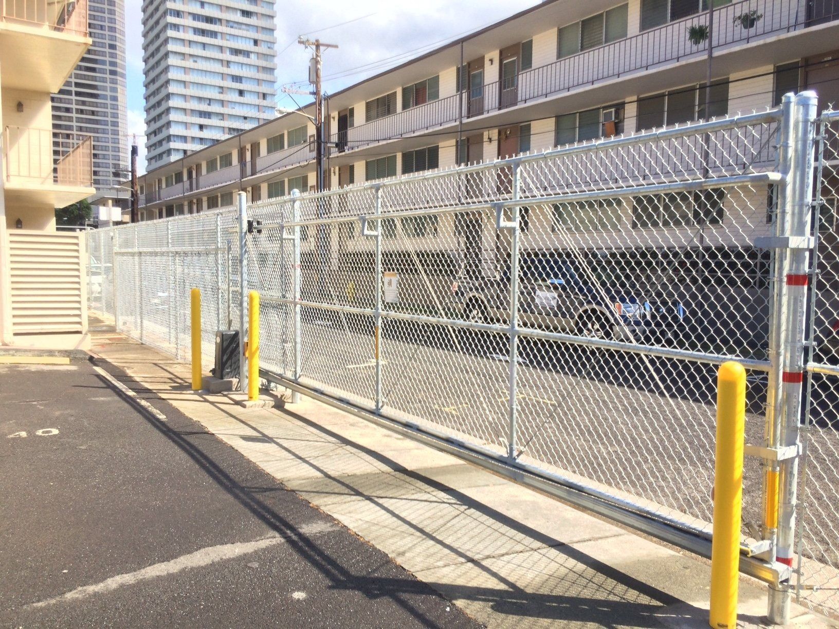 Chain link fence with sliding gate in front of a building and parking lot.