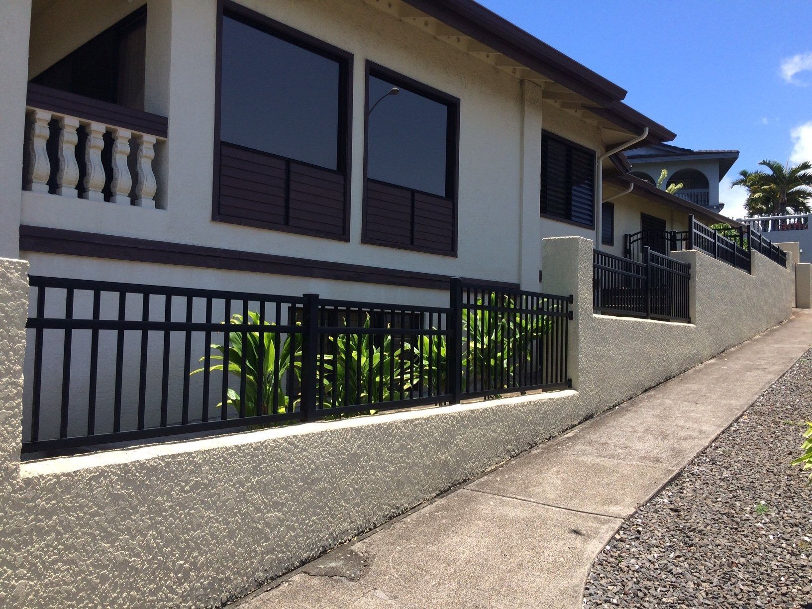 House with black fence and windows, and a concrete driveway.