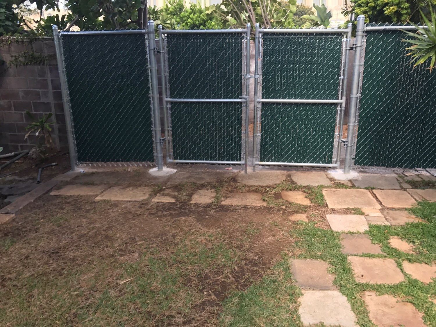 Green chain-link fence with gates on a stone path, in a yard.