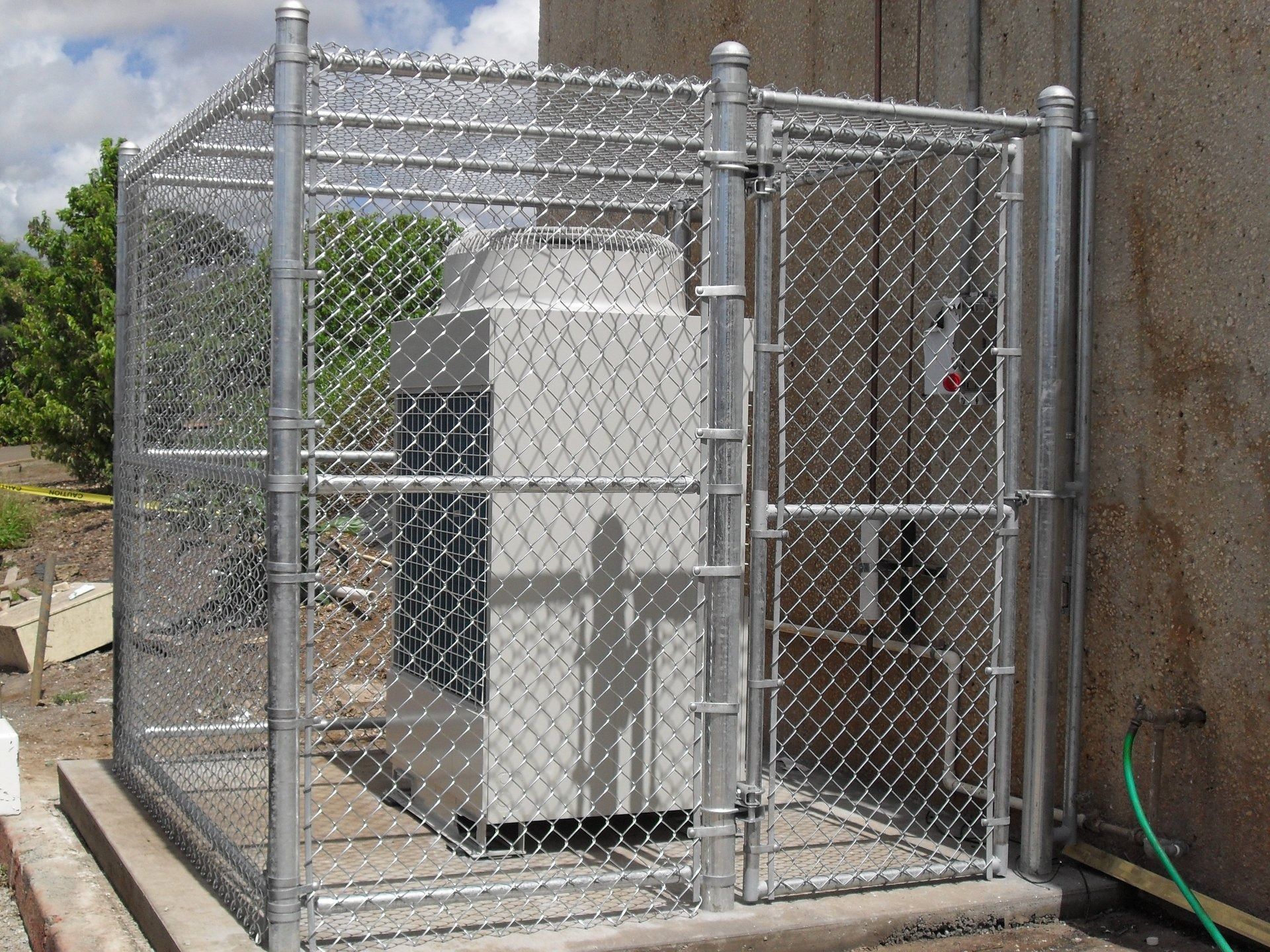 Chain-link fence enclosure around a large, rectangular machine. It's next to a building.