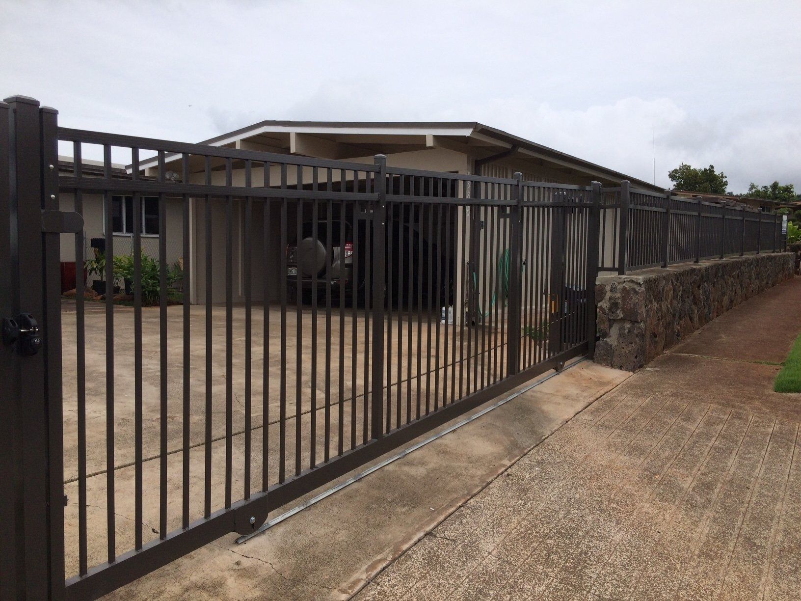 Dark metal gate and fence enclosing a house with a beige exterior, on a cloudy day.