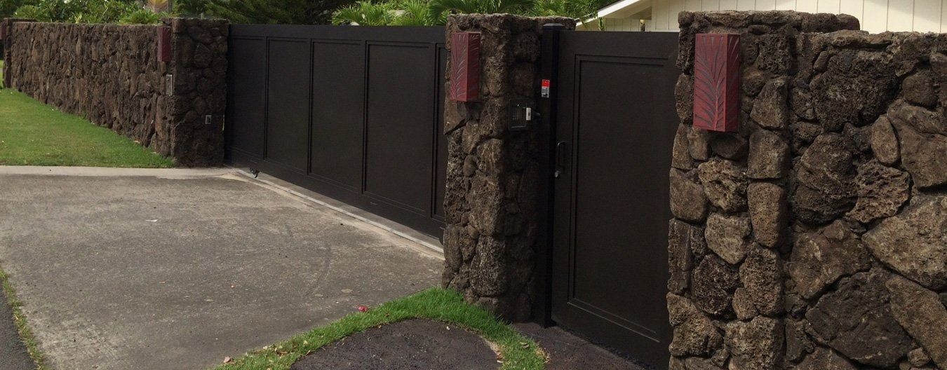 Stone wall with dark gate and mailbox. Concrete driveway and green grass in the foreground.