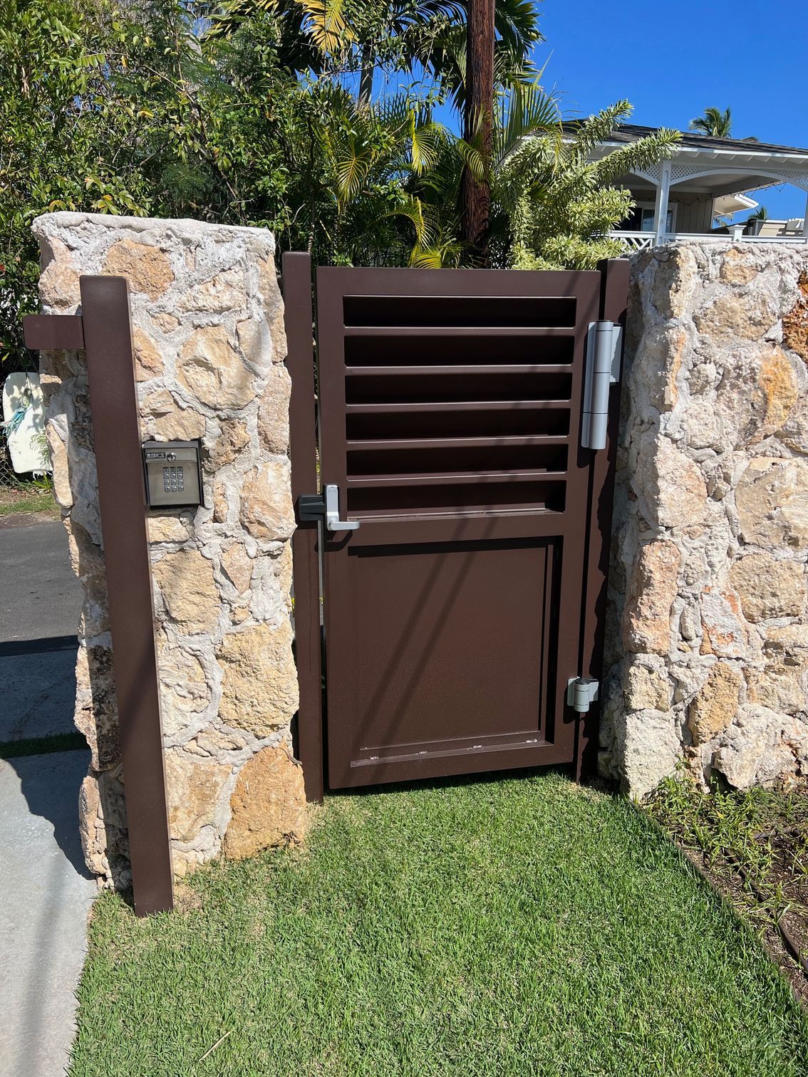 Brown metal gate set in a stone wall, with a mailbox and grassy area.