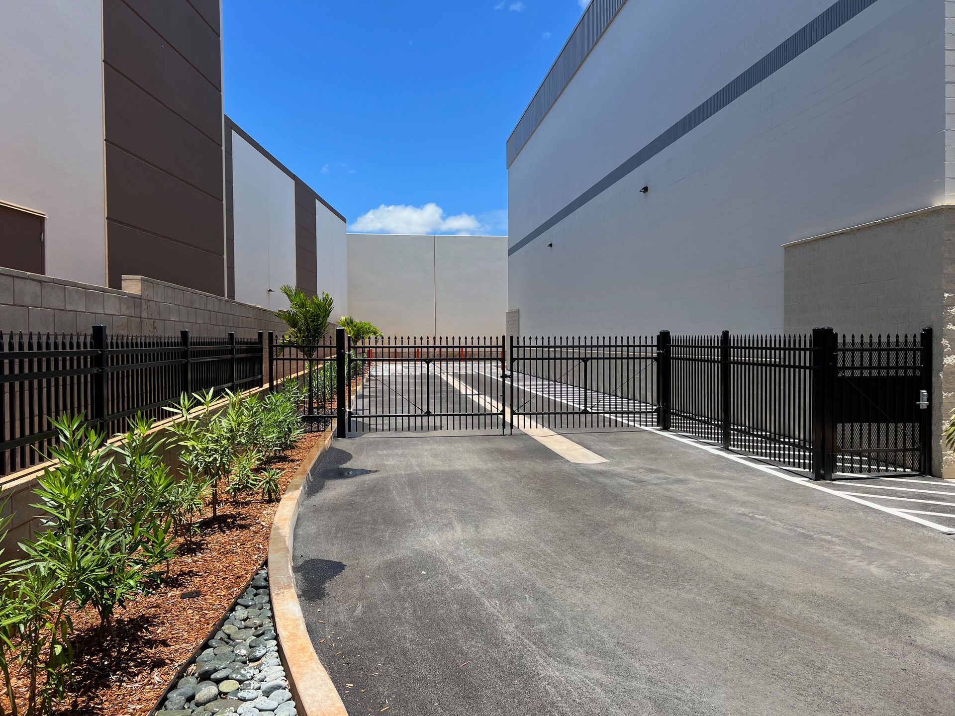 Black gate in paved lot between two large buildings, under a blue sky.