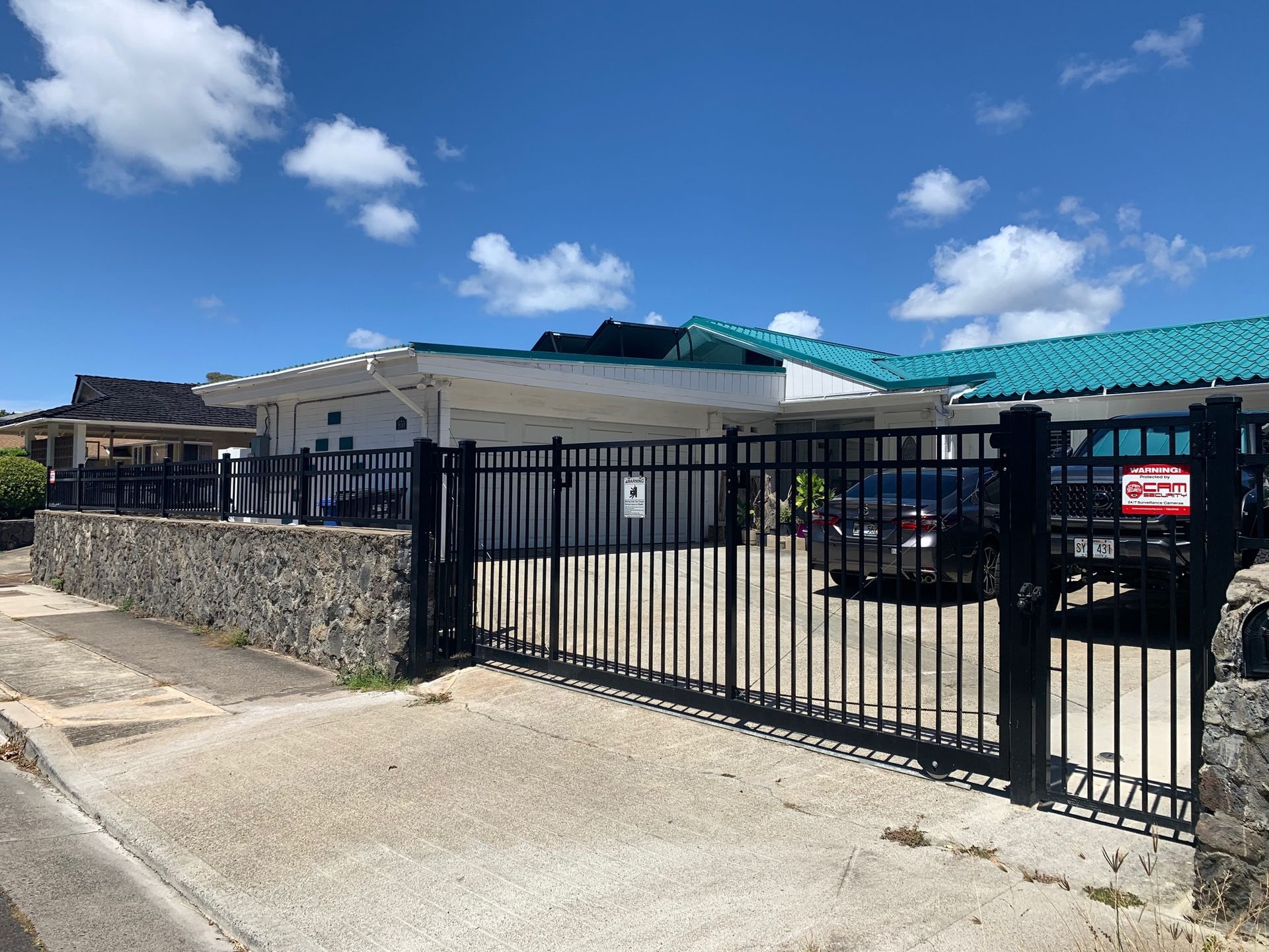 Black gate and fence in front of a house, stone wall, blue sky, concrete, car.