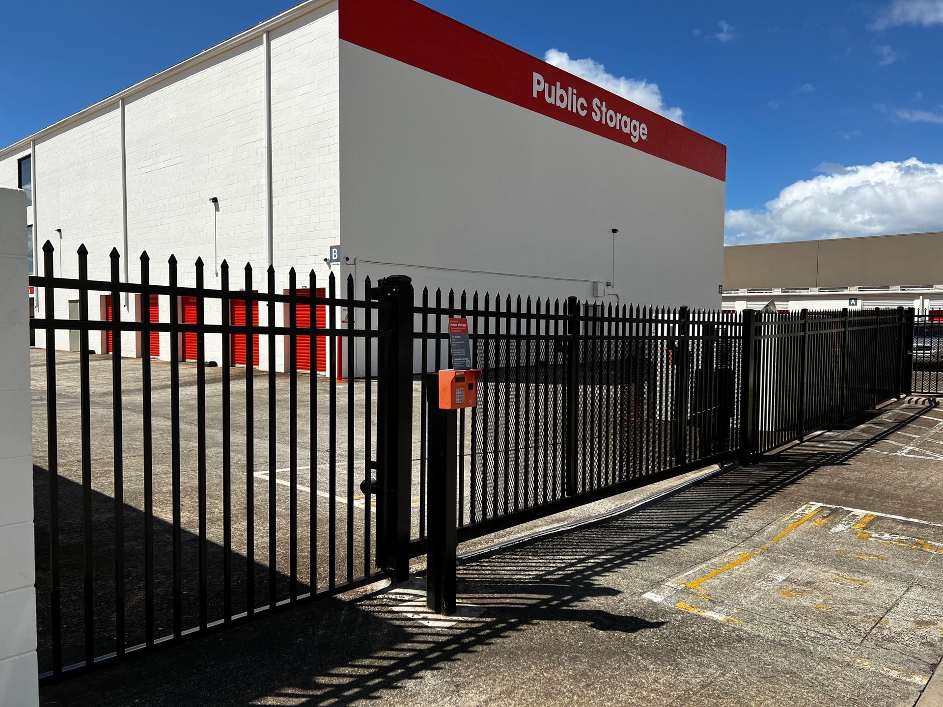 Black fence and gate in front of a Public Storage building with red doors.