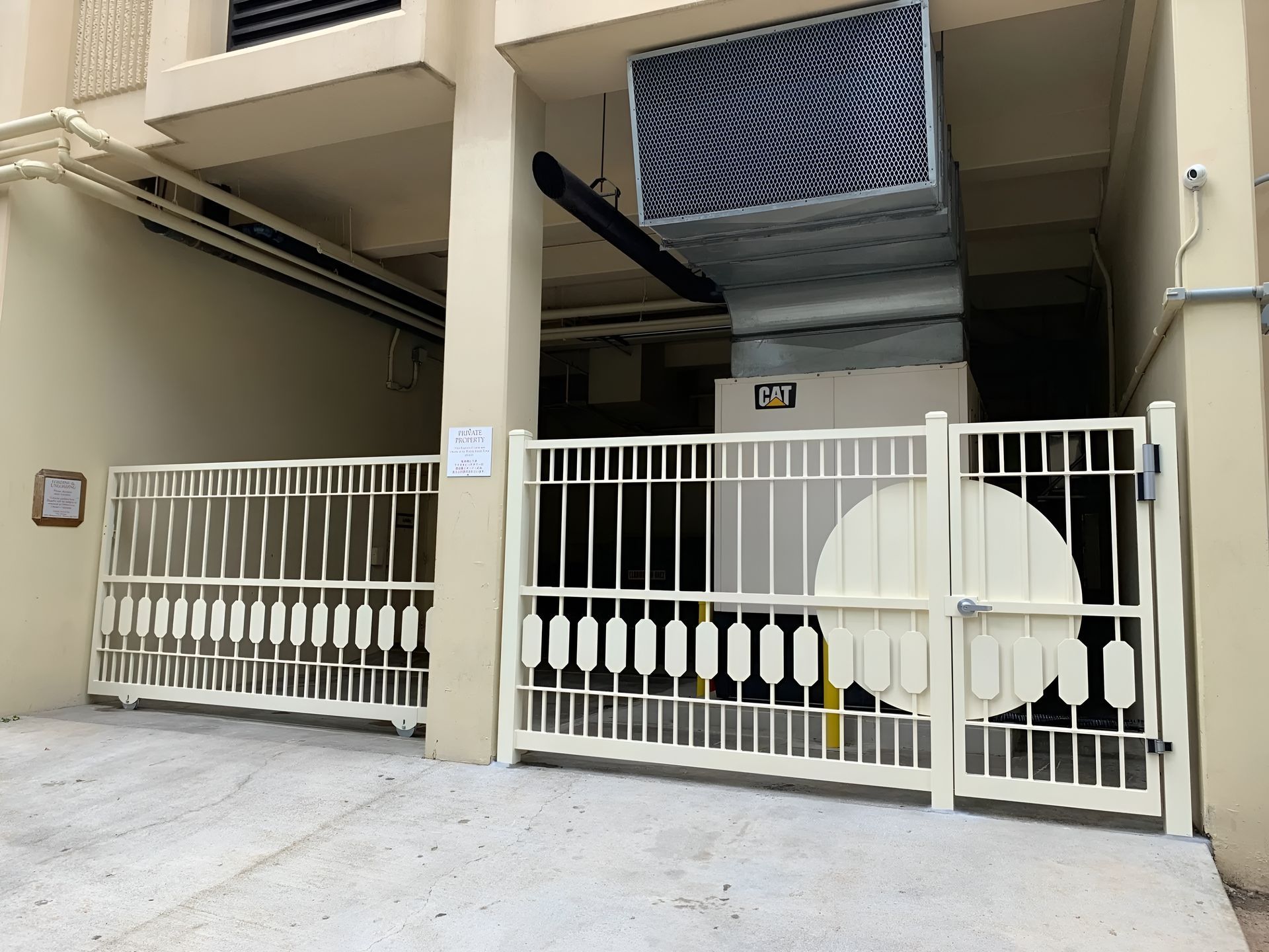 Beige metal gates in front of a building with an air conditioning unit and beige pillars.