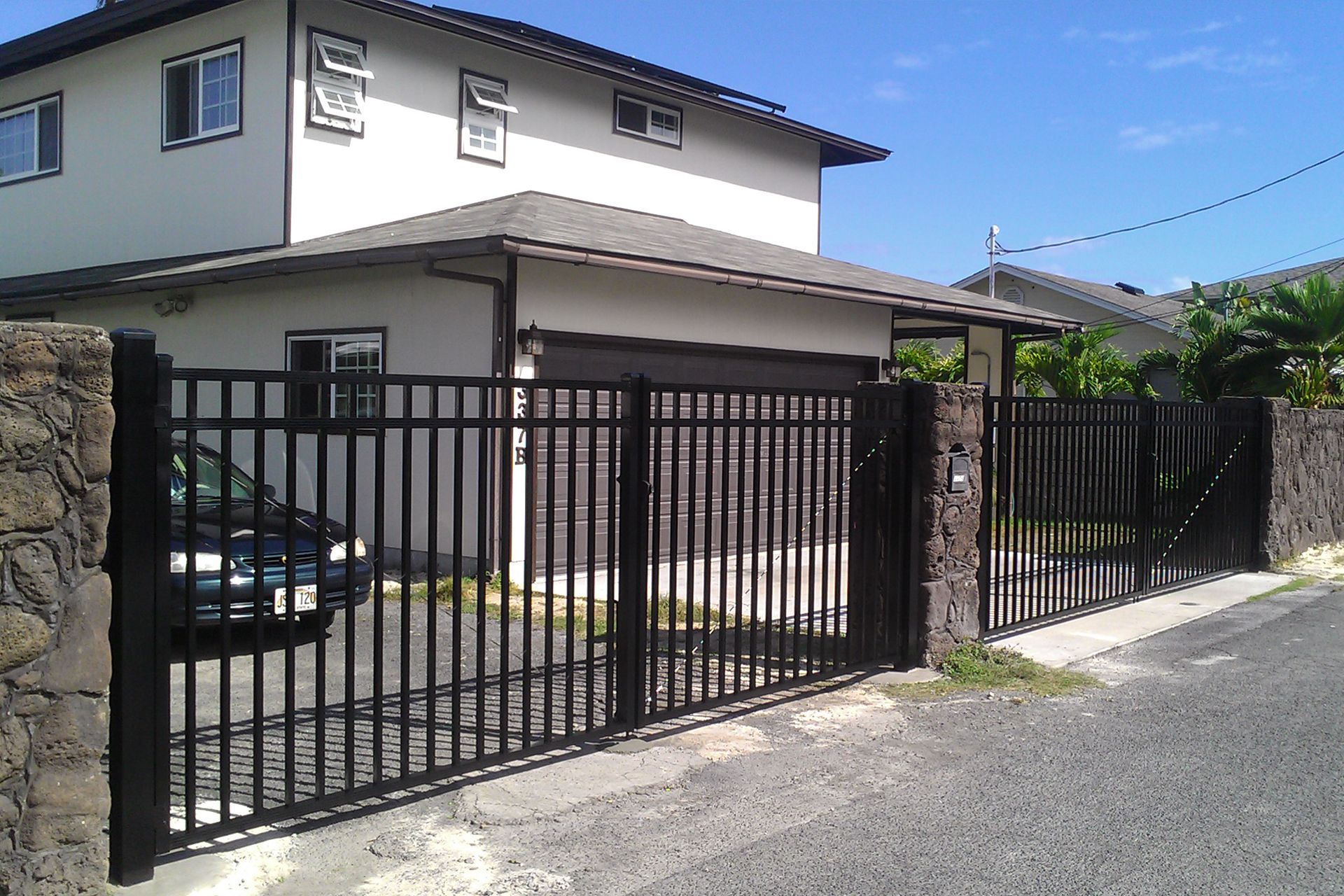 Black metal gate in front of a light-colored two-story house with a driveway and garage.