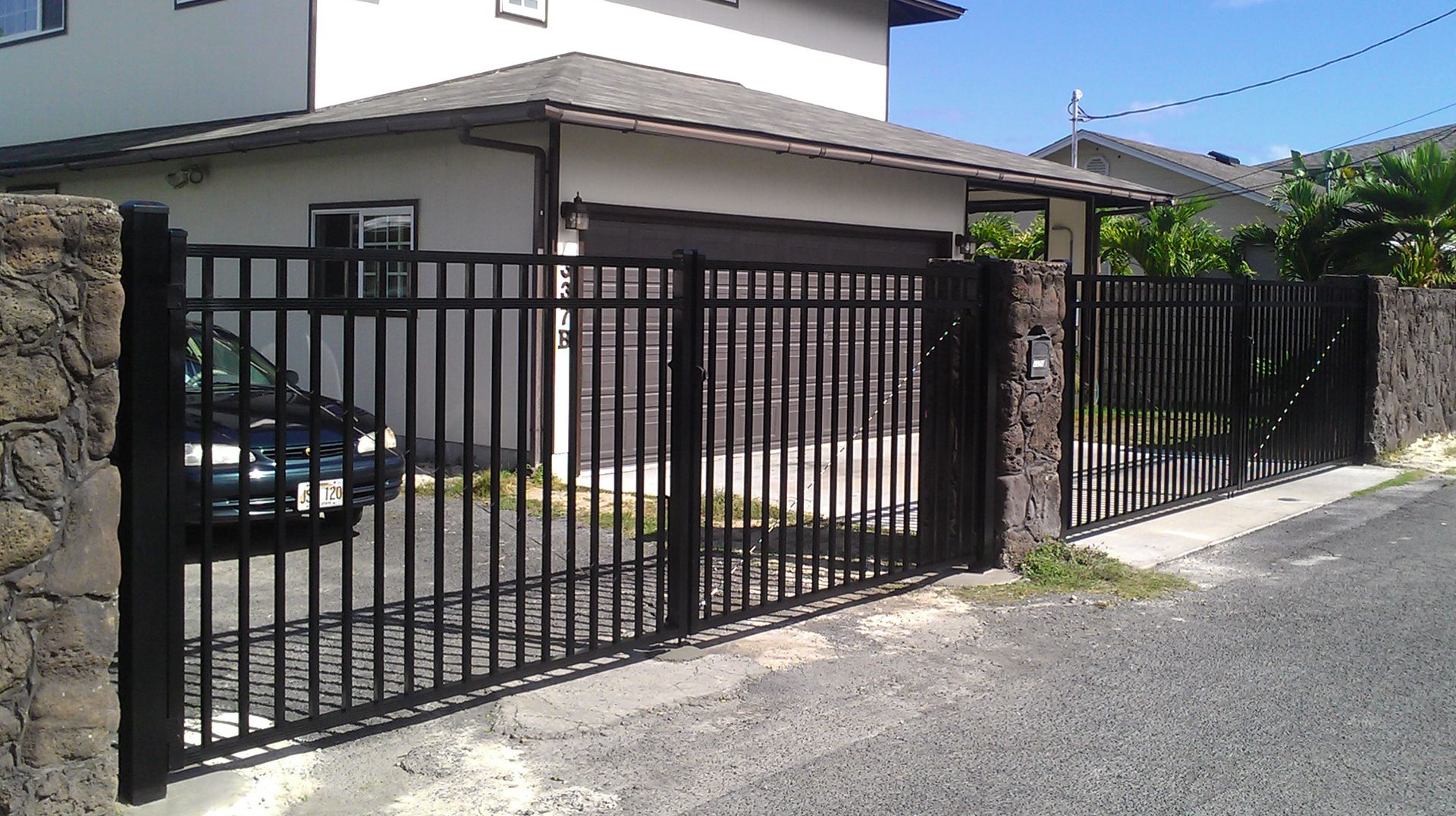 Black metal gate and fence in front of a house. A car is visible behind the gate.