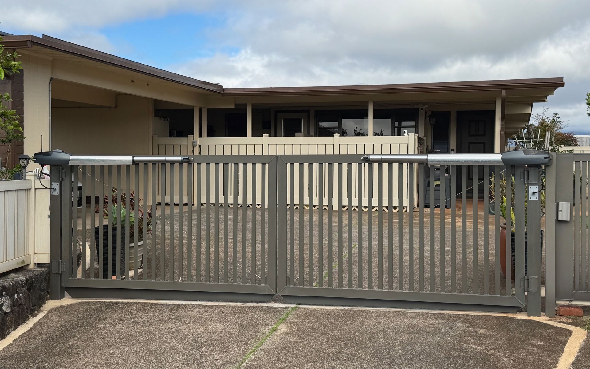 Gray metal front gate of a house with a covered carport and cloudy sky overhead