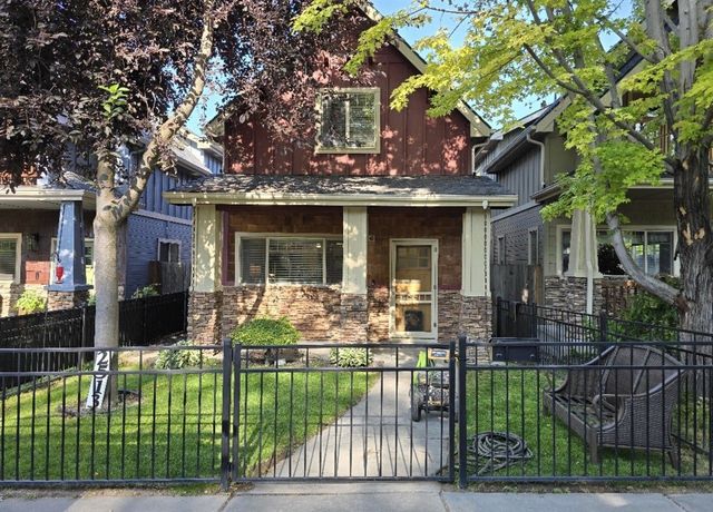 Small house with red upper story, stone porch, front yard, and black metal fence under leafy trees