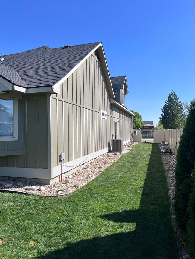 Side view of a beige house with a gray roof and narrow green lawn under a clear blue sky