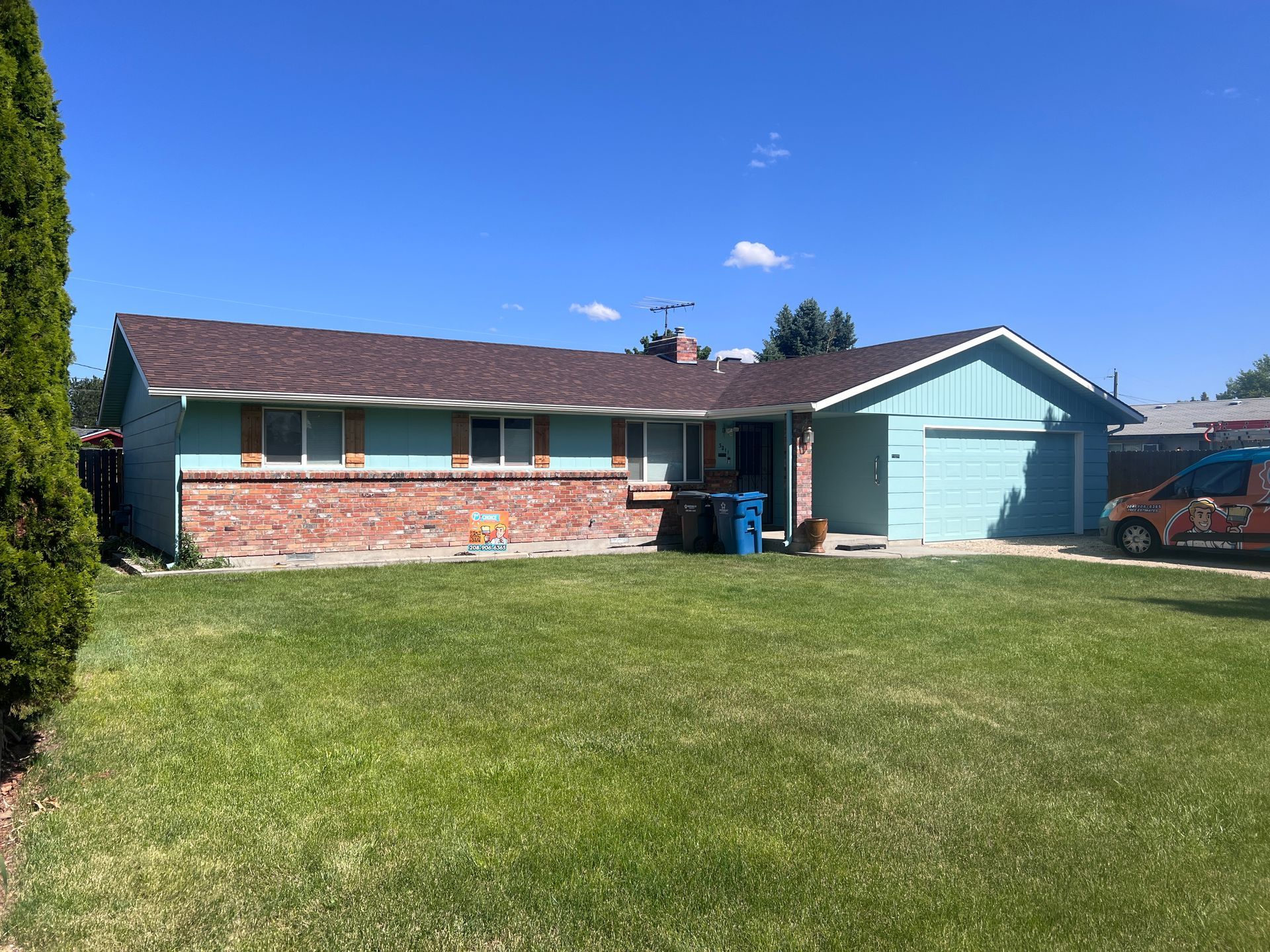 Single-story brick house with teal garage and wide green lawn under a clear blue sky