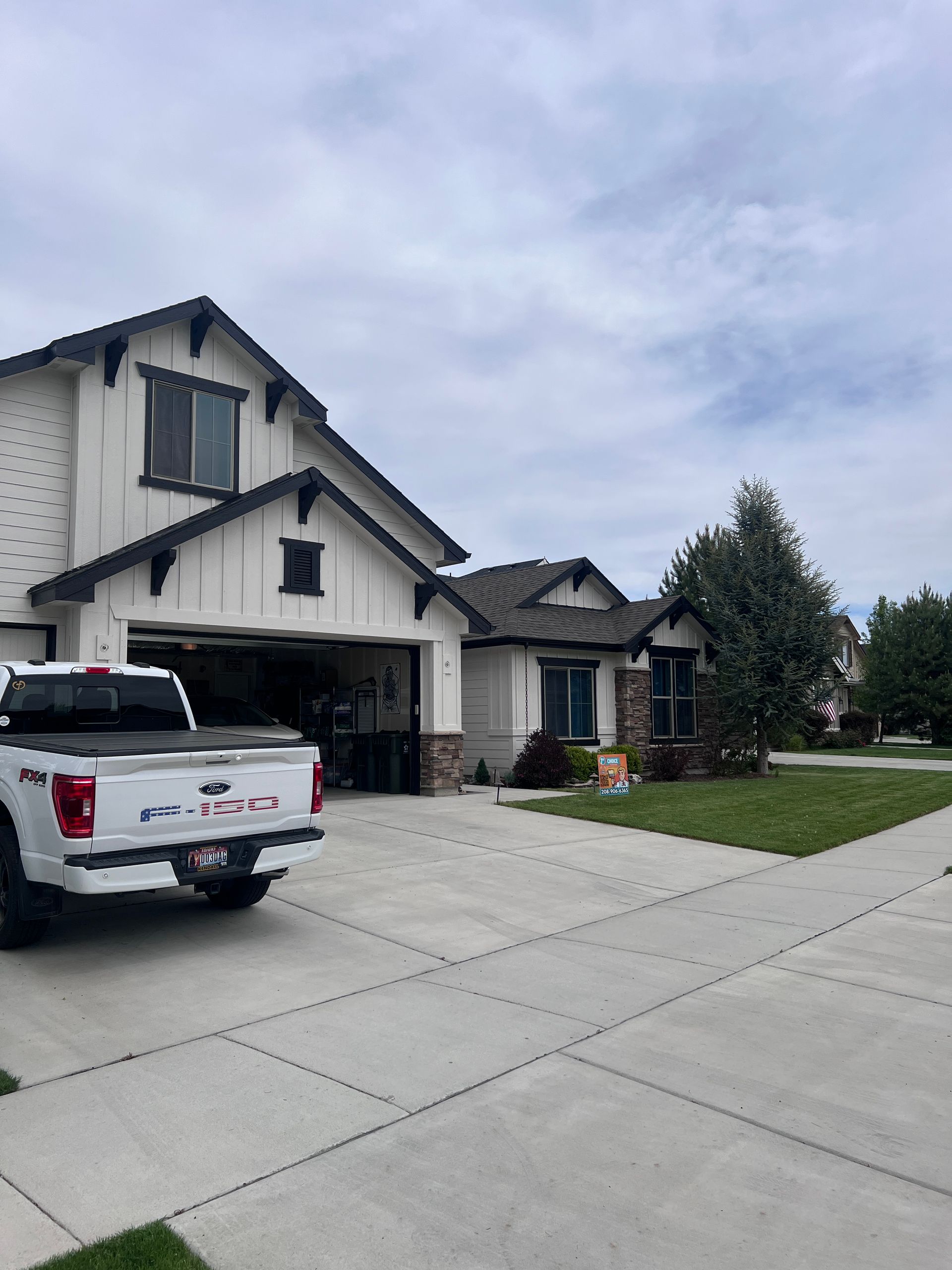 Suburban house with white pickup in driveway and a green lawn under cloudy sky