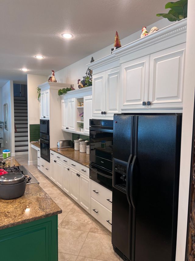 Bright kitchen with white cabinets, black refrigerator, and green island on granite counters