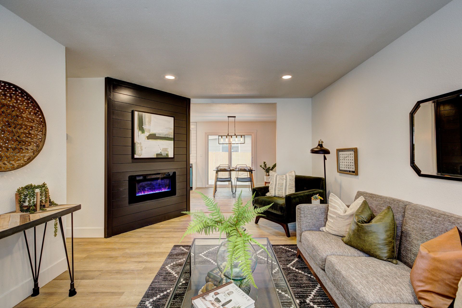 Modern living room with gray sofa, fireplace, wall art, and light wood floors opening to a dining area