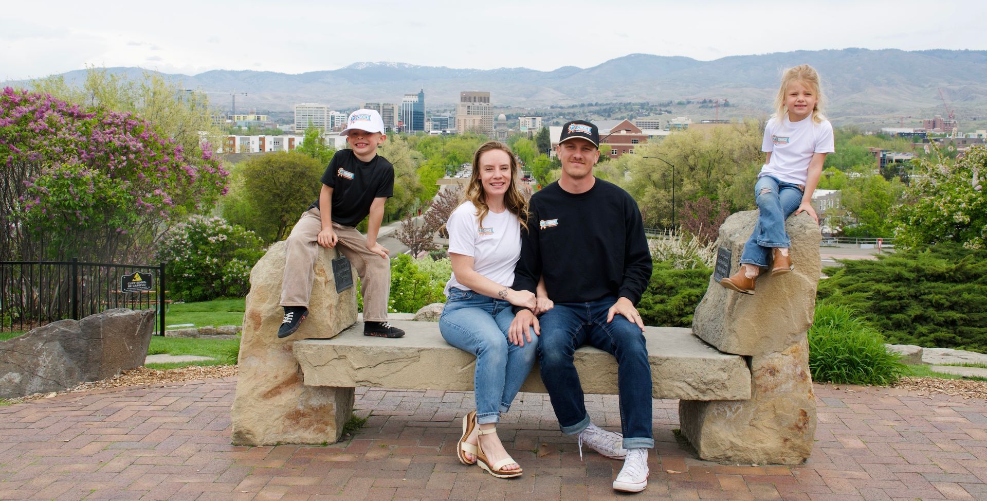 Family sitting on a stone bench at a scenic overlook with mountains and city in the background