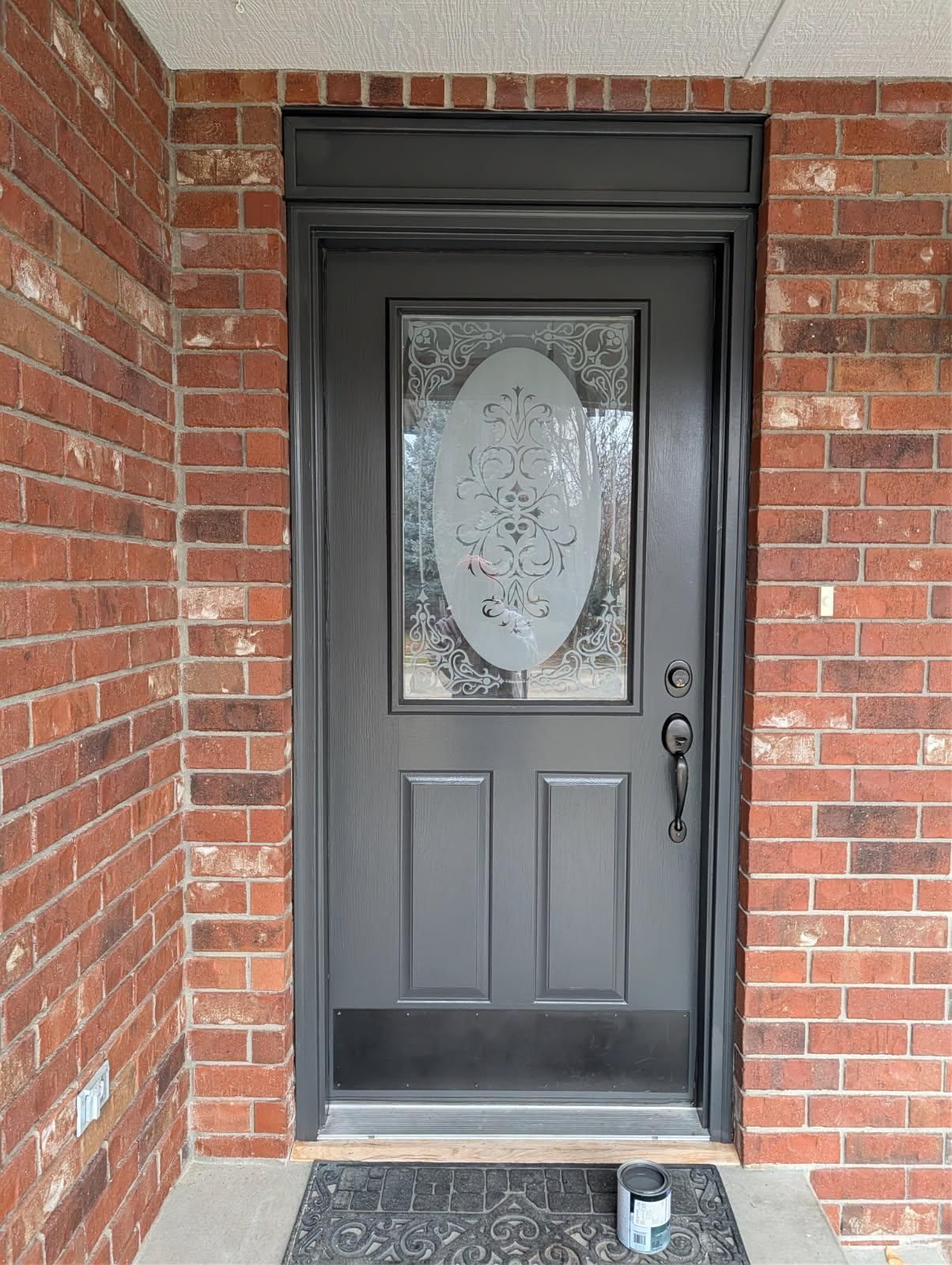 Black front door with oval frosted glass in a red brick entryway