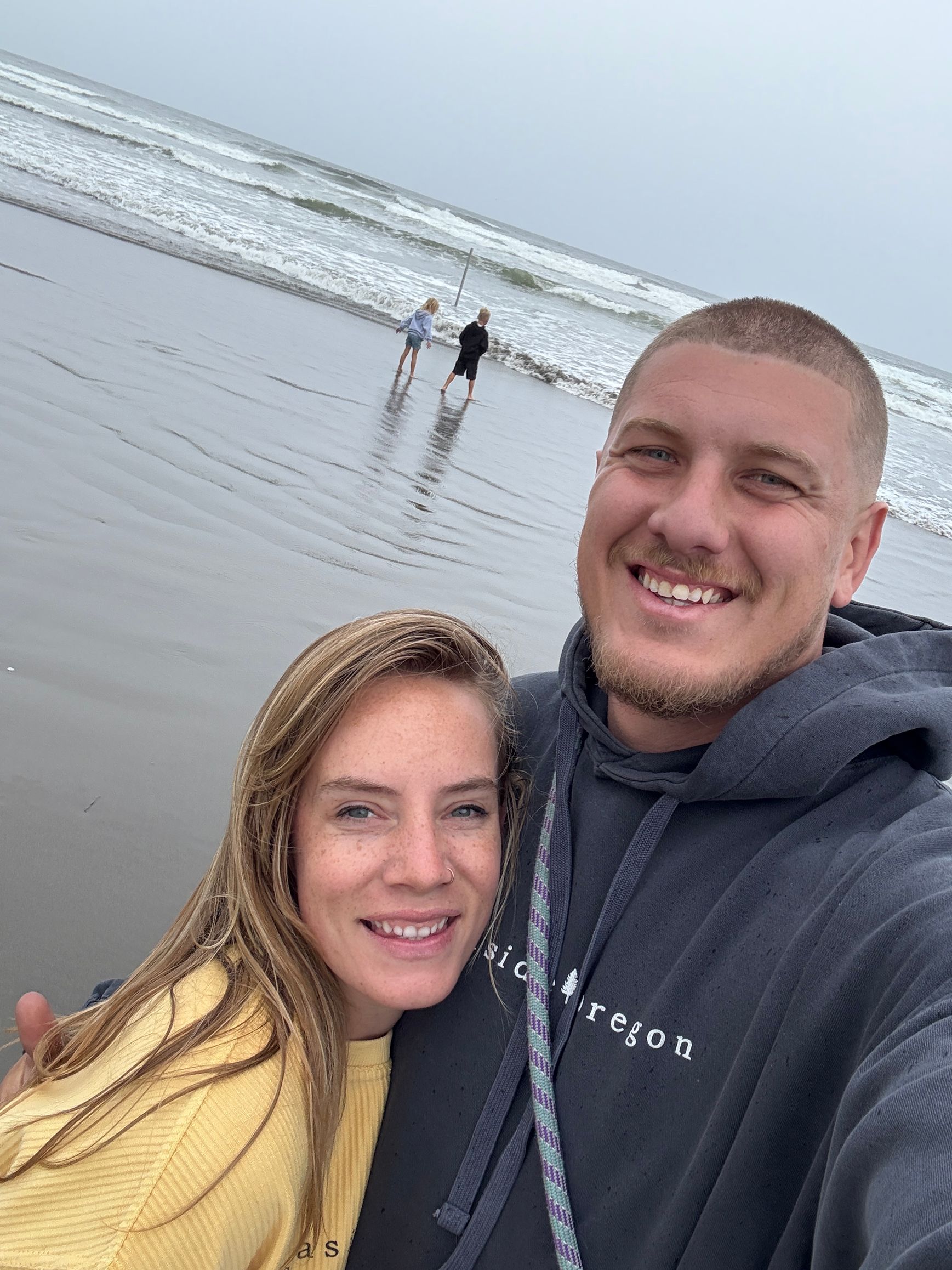 Smiling couple taking a selfie on a cloudy beach with waves in the background