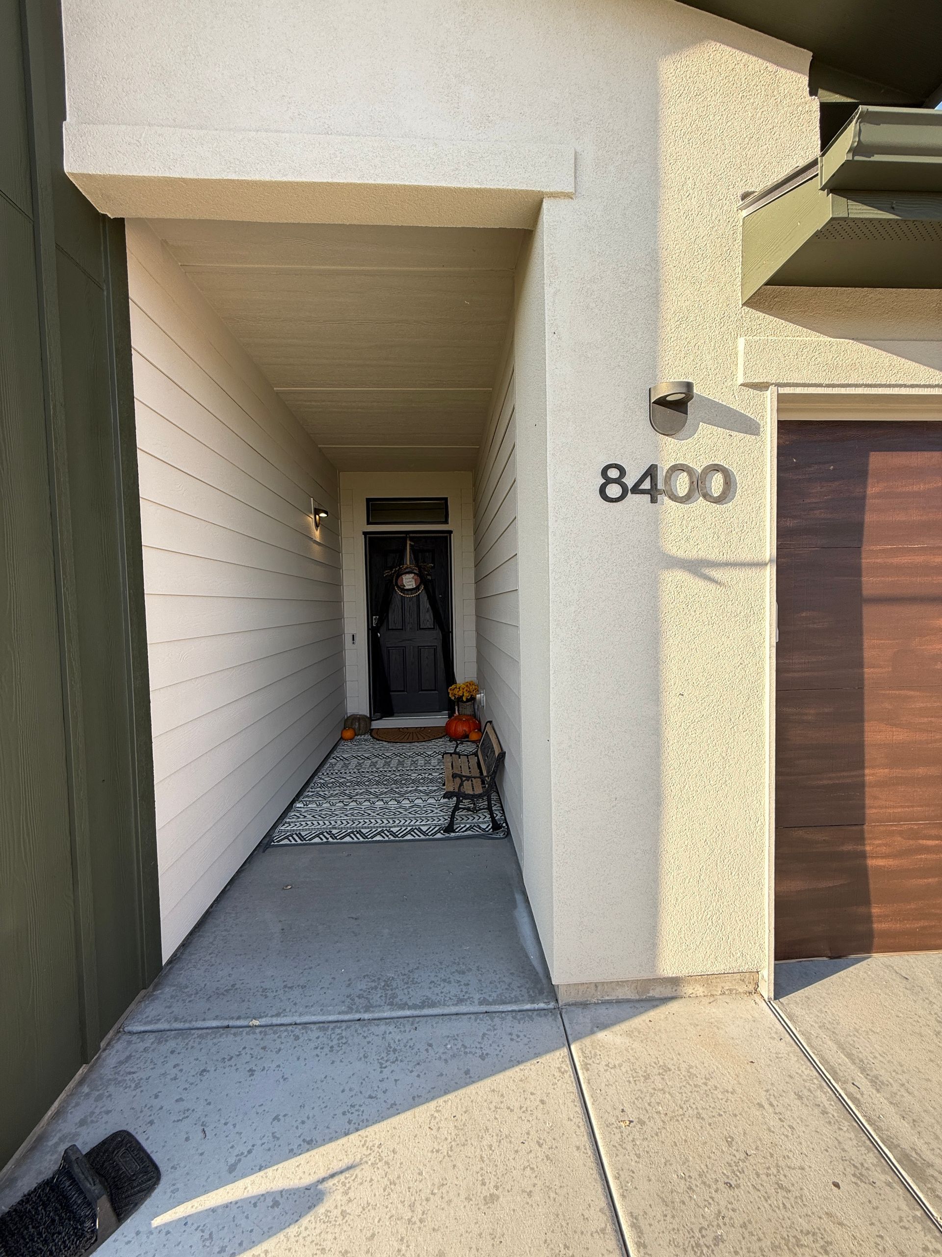 Front entryway of a house with a concrete walkway, house number 8400, and a Halloween decoration by the door
